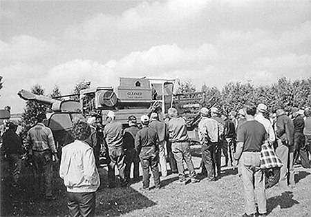 A group of people look at a piece of farm machinery.