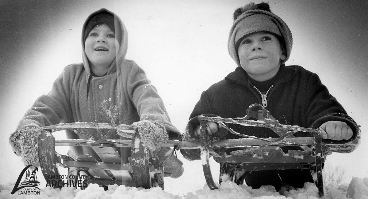 Black and white image of two children on a sled in the snow.