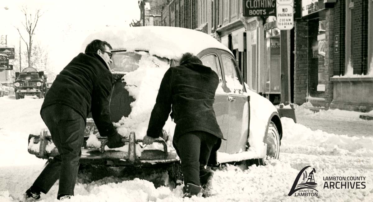 Image of two men pushing a car in the snow.