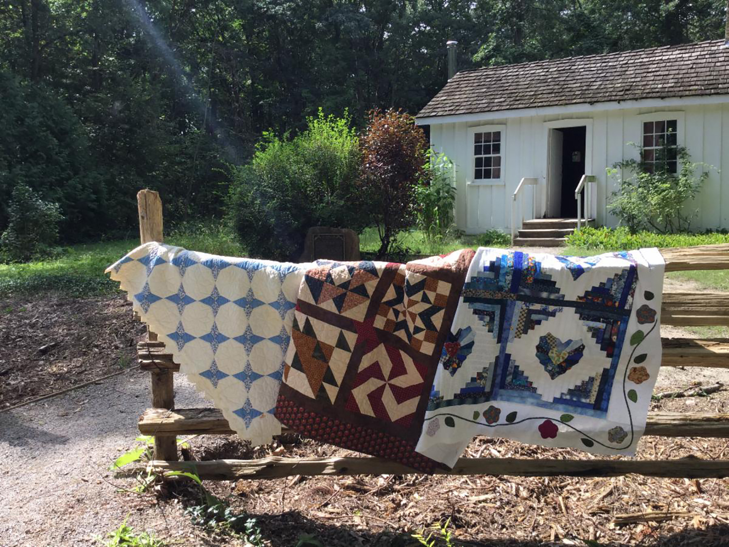 Quilts from the North Lambton Quilter's Guild hanging over fence in front of Tudhop house.