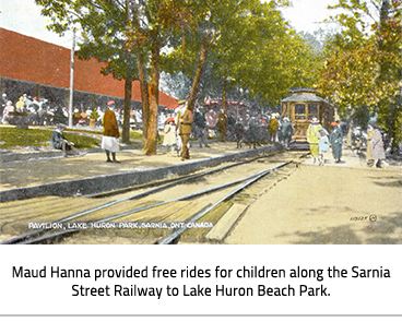 (The Sarnia Street Railway. A busy day with lots of people in the park, the brown rail way car sits on its tracks. To the left is a building with a red roof. Image Caption: "Maud Hanna provided free rides for children along the Sarnia Street Railway to Lake Huron Beach Park."), link.