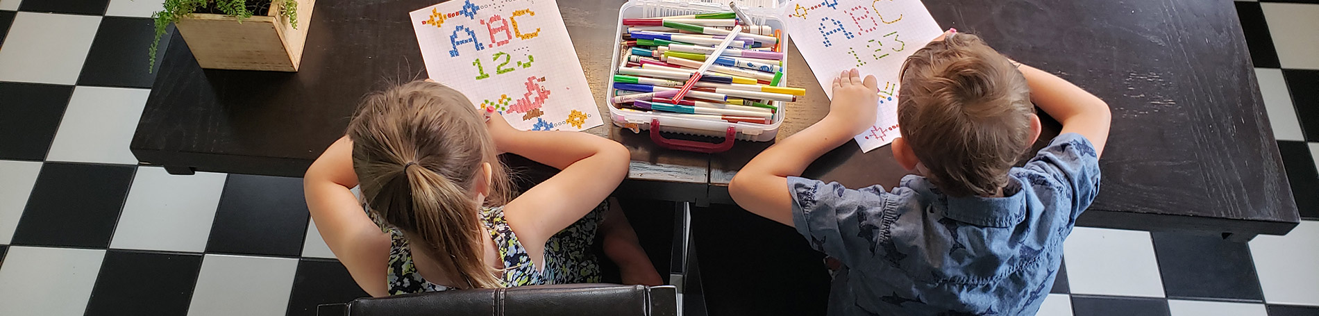 Two children sitting at a table with markers and paper.