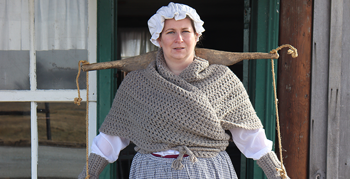 Lady wearing a bonnet standing with a piece of wood across her shoulders.