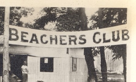 A sepia-toned, faded photograph of a cabin-like building surrounded by a few tall trees. A man stands in front of the building. A label reading Beachers Club has been embossed over the photograph.