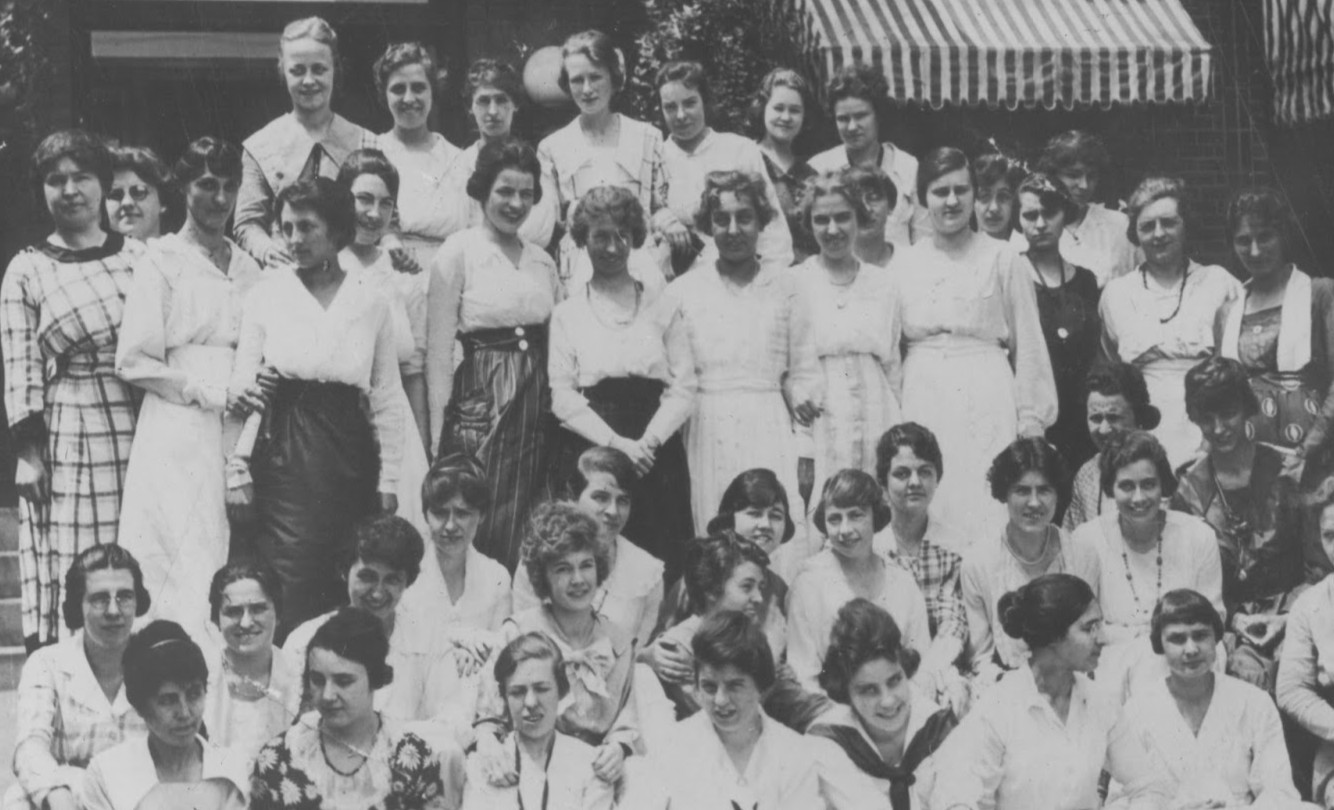 A large group of women, dressed in early 20th-century attire, pose together outside a building with striped awnings, identified as the female staff of the Imperial Oil Company in Sarnia, 1919.