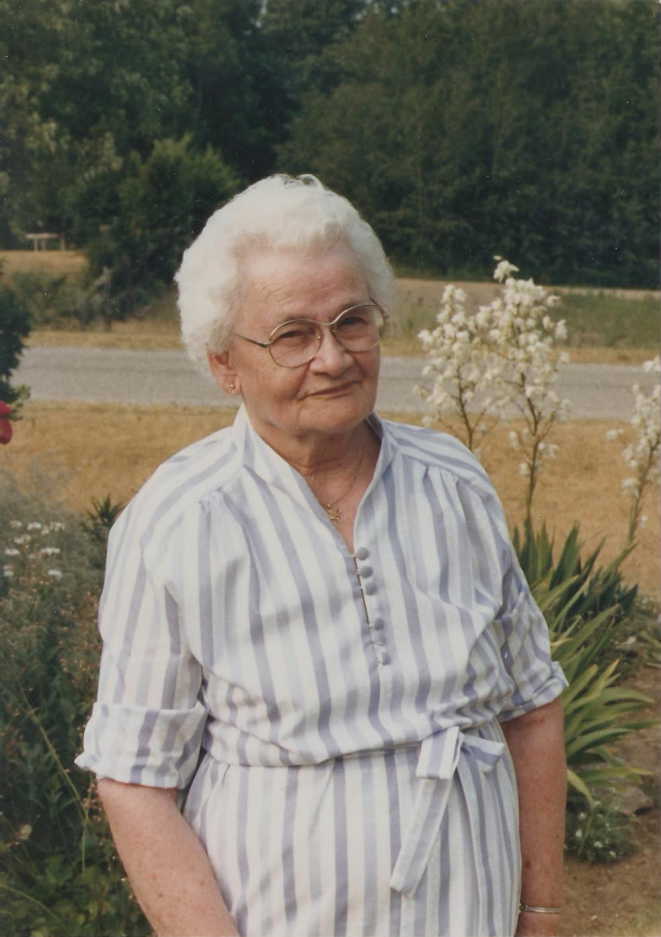 elderly woman standing in front of wooded area, outside