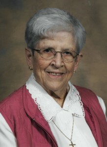 White woman with grey hair and glasses wearing a white long sleeve with a pink vest.