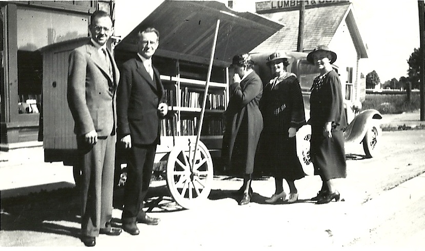 Black and white image of four three women and two men standing in front of a mobile library.