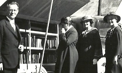 Black and white image of four three women and two men standing in front of a mobile library.