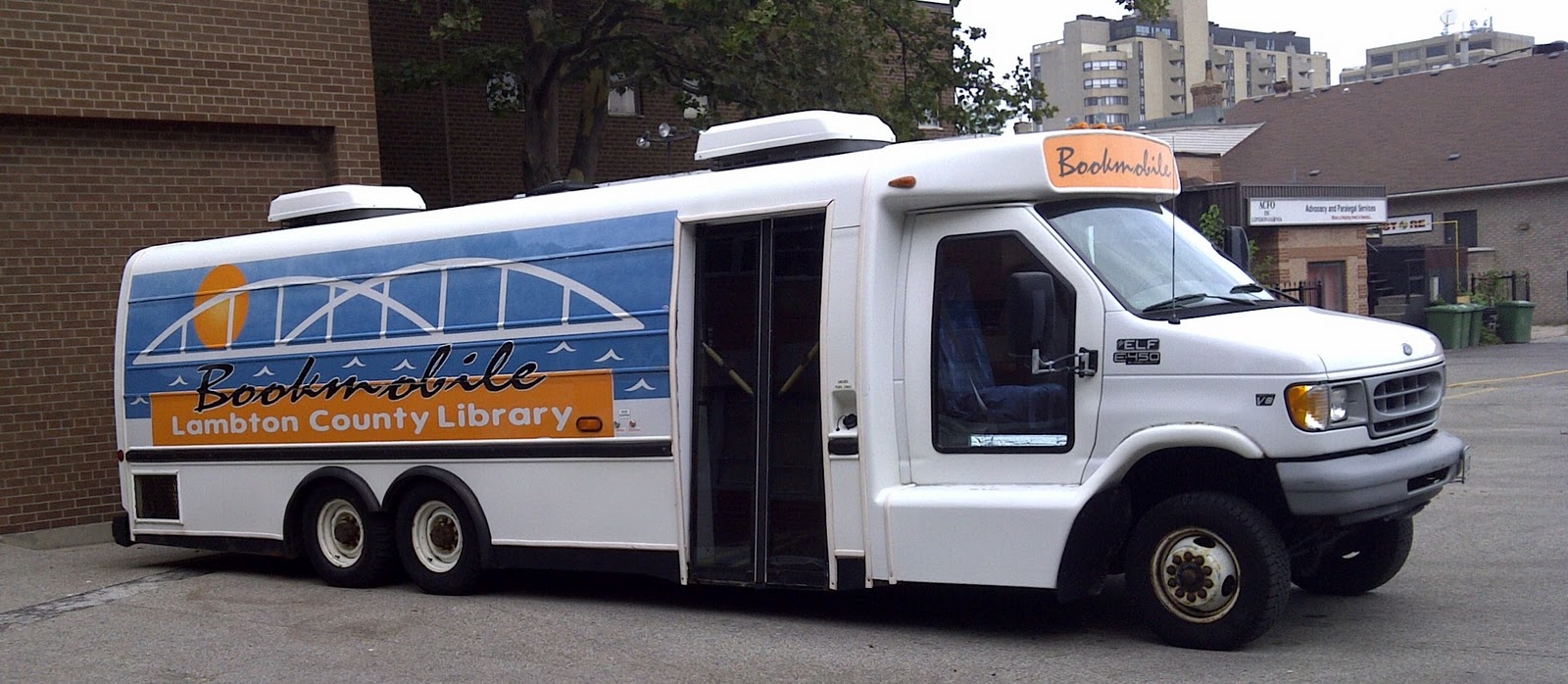 Long white van in front of a brick building.