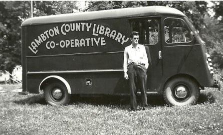 Black and white image of a man standing in front of a van.