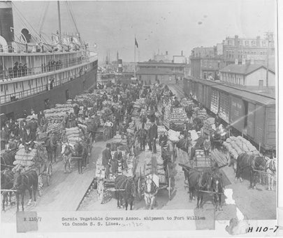 Black and white image of vendors beside a docked ship.