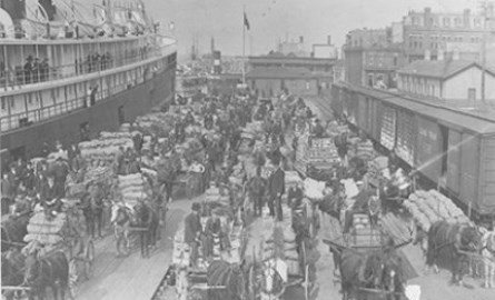 Black and white image of vendors on a dock next to a ship.