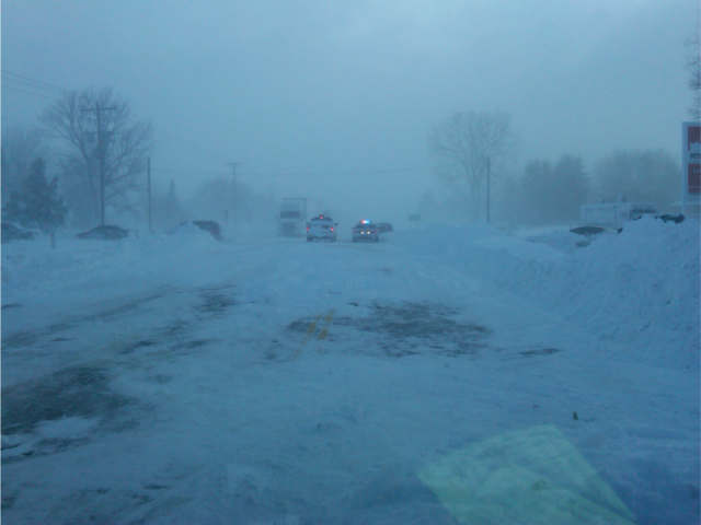 Police cars on a road with vehicles crashed in a snowstorm.