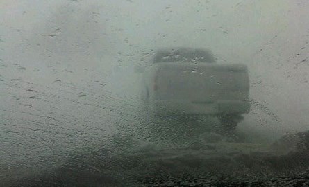 View from windshield in a snowstorm with a truck in front.