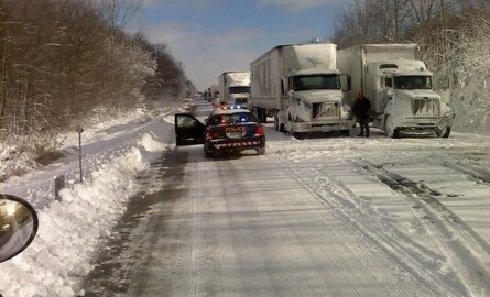 Police car and transport trucks parked on the side of a snowy road.
