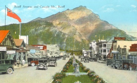 Old cars parked in front of tents and a mountain.