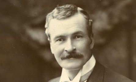A well-dressed man with a mustache poses confidently in a formal studio portrait from the late 19th or early 20th century.