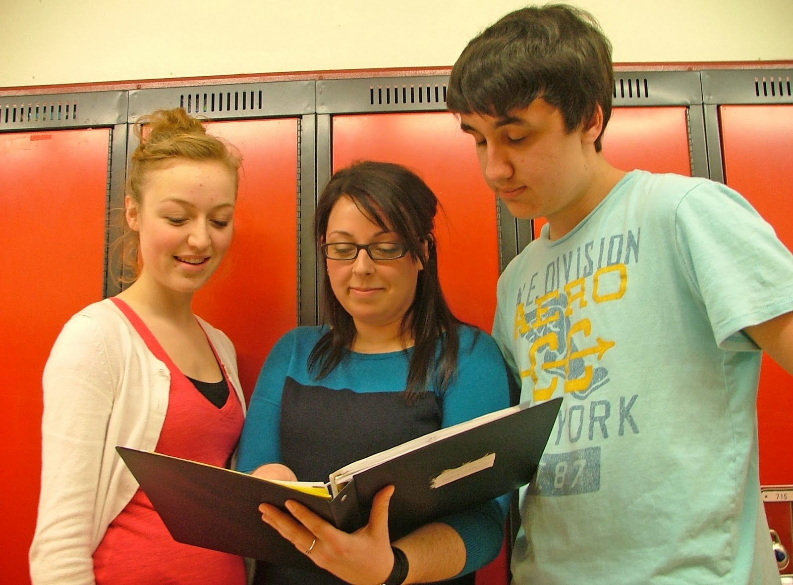 Women standing in front of lockers looking at a book with two students.