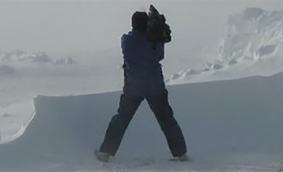 Man with a video camera stands on an icy landscape.