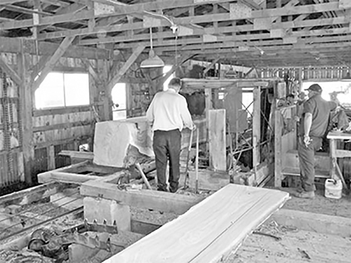 Carlyle Searson is operating a steam-powered saw, using scrap wood as fuel for the engine. 