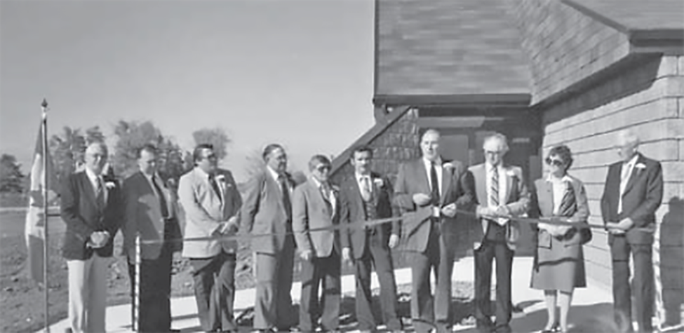 Opening of the township office on Nauvoo Rd., 9 men and one woman stand behind a ribbon.