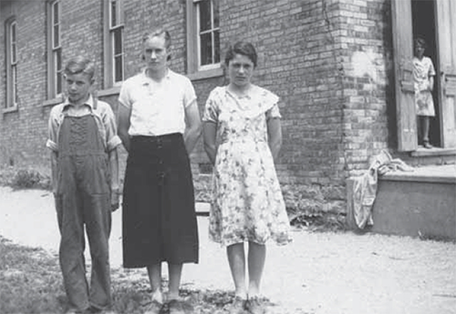 Two girls and one boy outside of a brick building.