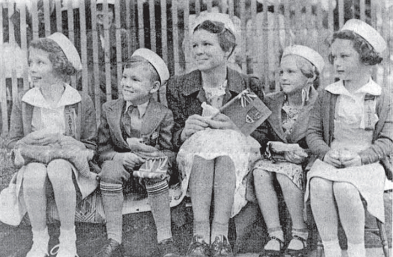 Four children and a woman sit on a curb for a parade.