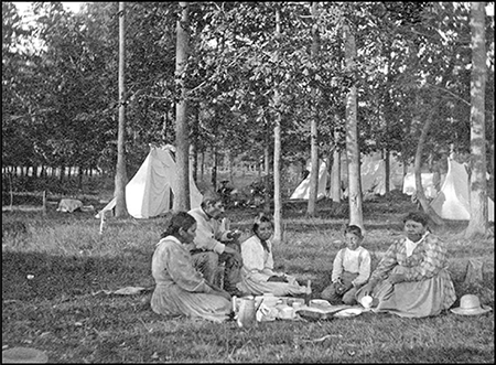 Indigenous family picnicking in front of a camp.