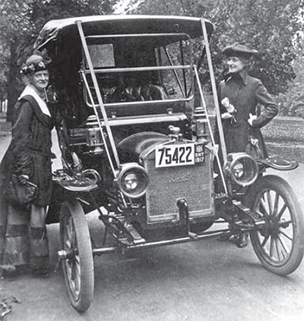 Two women stand on either side of a 1917 Overland car.