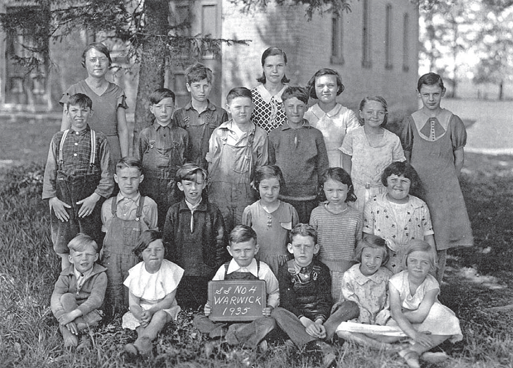 School photo of children and teacher outstide of a school house.