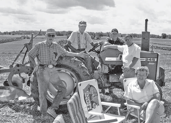 Four men stand around a tractor, a woman sits in front.