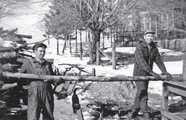 Carl and LLoyd Bryson cutting wood from a pile on a table.