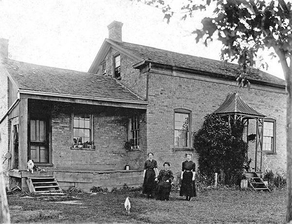 Mary Ann McChesney with daughters stand in front of a large brick house.