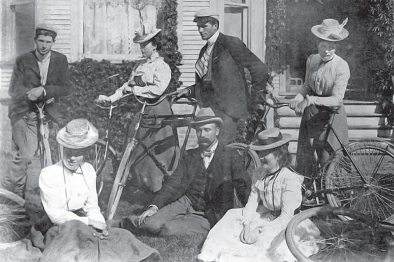 A group of people sitting outside and standing with bikes.