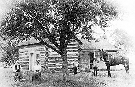 Log home with people out front, one has a horse.