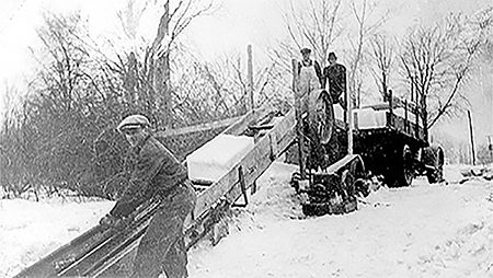 Ice is loaded onto a truck using a ramp-pulley system.