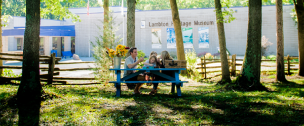 A family sits at a picnic table in front of the Lambton Heritage Museum