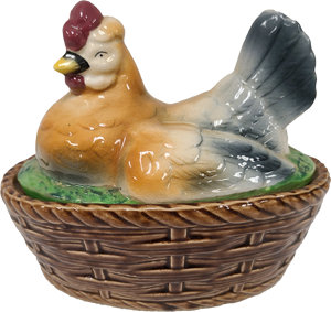 A ceramic orange, white and blue hen with a yellow beak and red wattles. The hen sits on a ceramic brown basket that is made to look woven.