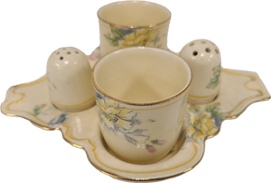 A cream tray with two matching cups and salt and pepper shakers. There is a gold around the edges and a floral pattern.