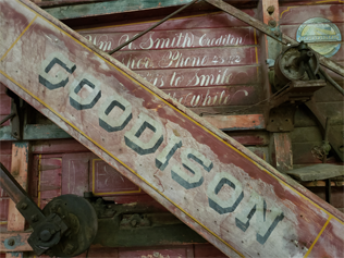 Close up of the side of the Goodison Thresher showing a diagonal beam that says "GOODISON" and obscures cursive text behind it.