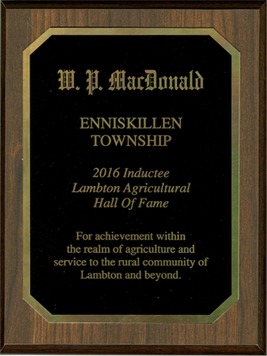 A wooden plack with metal accents that reads "W.P. MacDonald Enniskilledm Township 2016 Inductee Lambton Agricultural Hall of Fame For achievement within the realm of agriculture and service to the rural community of Lambton and beyond."