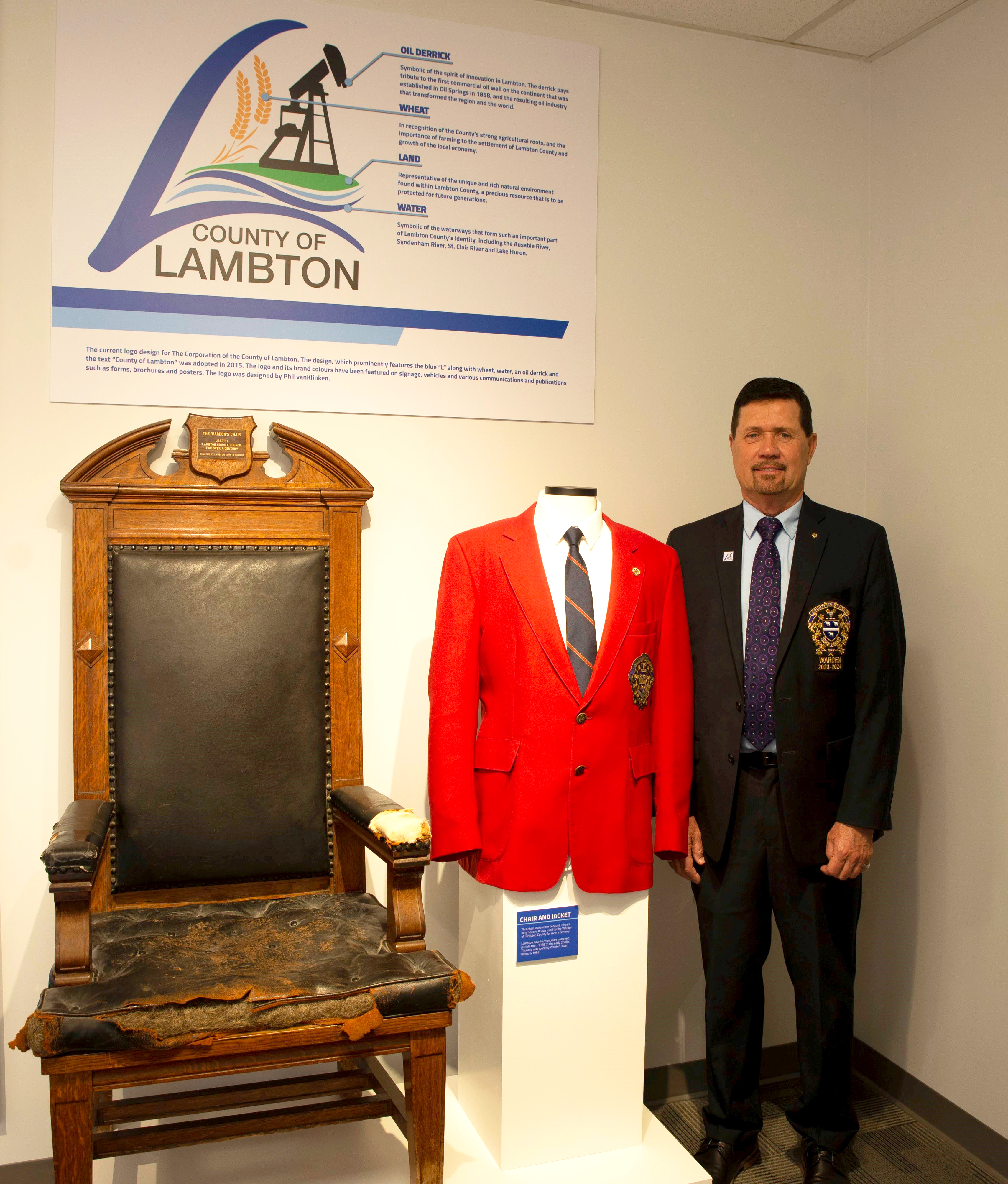 Warden Kevin Marriott posing next to the former Warden's Chair and Jacket