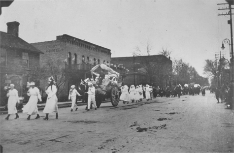 Men and women marching down a road with a parade float, link.