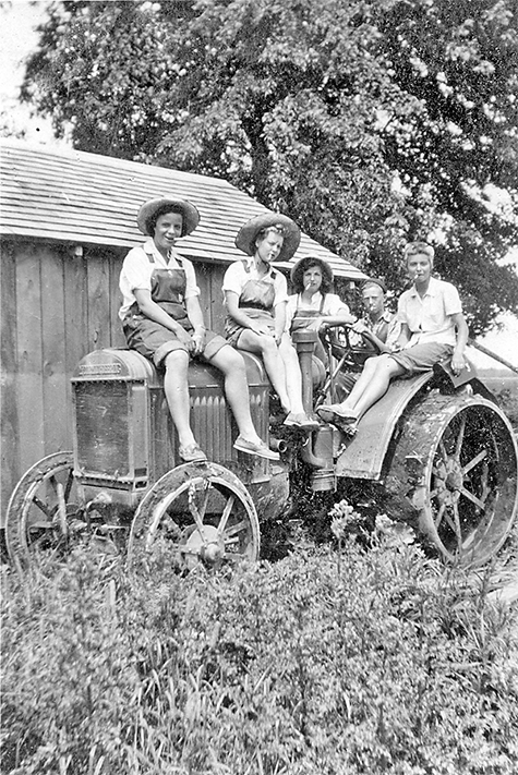 Farmerettes sitting on a tractor with a farmer.