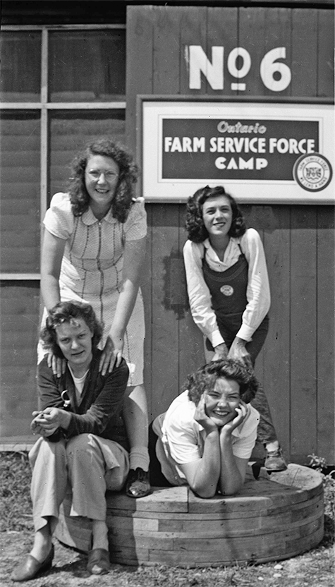 Four Farmerettes stand in front of the Thedford Camp sign.