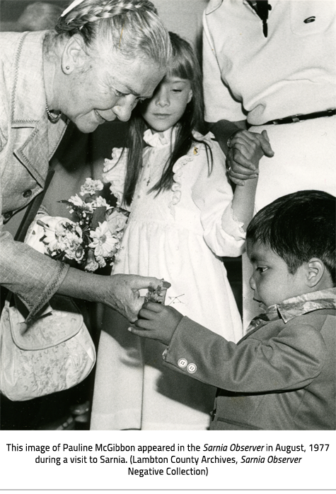 (Pauline McGibbon looks at flowers that a child holds up. Image Caption:"This image of Pauline McGibbon appeared in the Sarnia Observer in August, 1977 during a visit to Sarnia. (Lambton County Archives, Sarnia Observer Negative Collection)"), link.