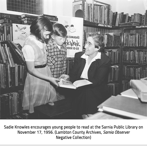 (Sadie in the library kneeling down to show two children something in a book. Image Caption: "Sadie Knowles encourages young people to read at the Sarnia Public Library on November 17, 1956. (Lambton County Archives, Sarnia Observer Negative Collection)"), link.