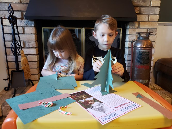 Two children sitting at a table cutting paper.