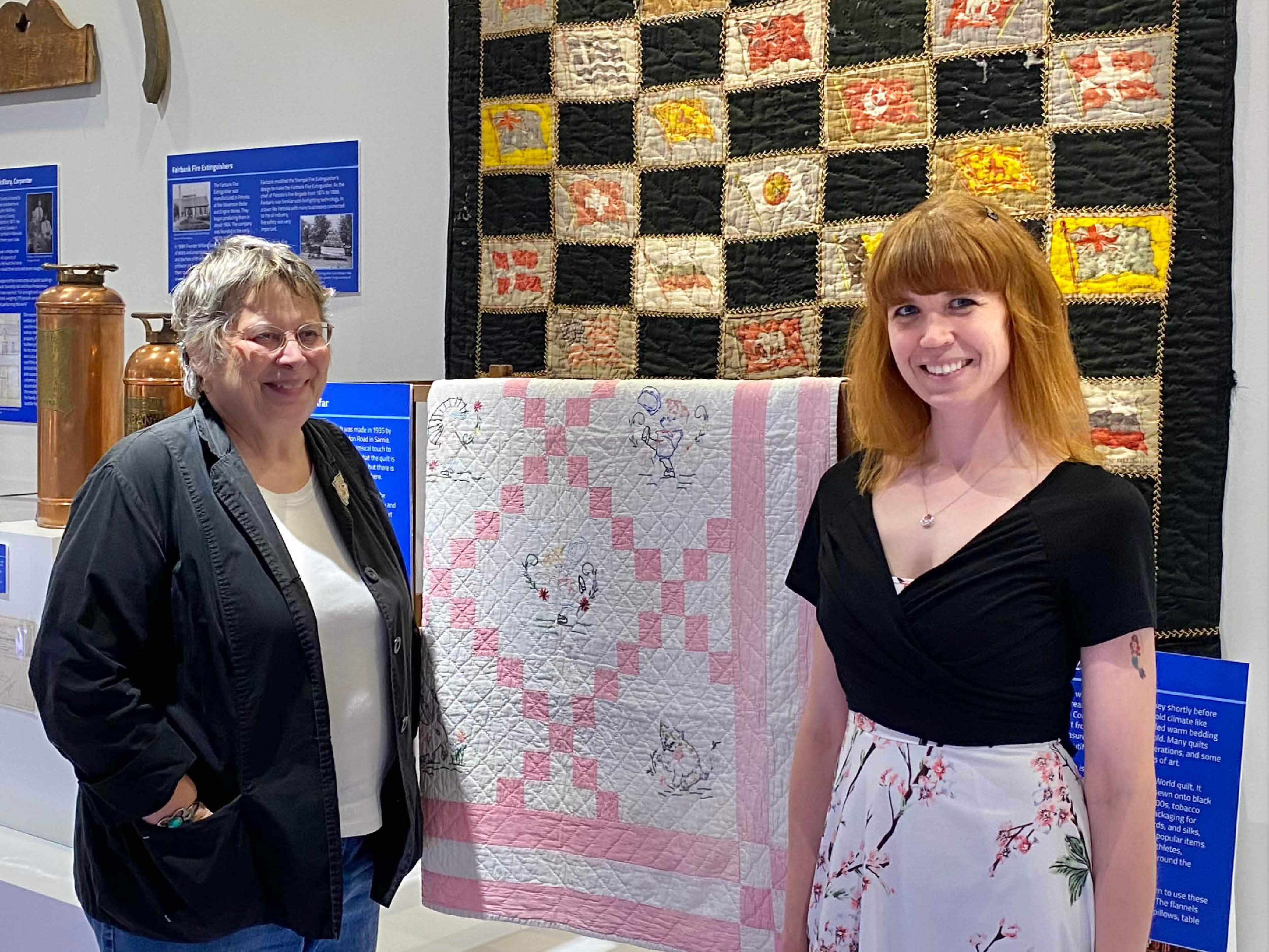 Guild Member Susan Hewett and Curator/Supervisor Dana Thorne stand before two quilts from the Museum's collection currently on display in the Lambton Gallery.